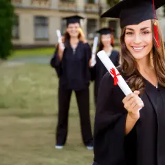 Absolventin mit Urkunde, bereit für MBA mit Fachwirt. Mehrere Studenten in Roben im Hintergrund.