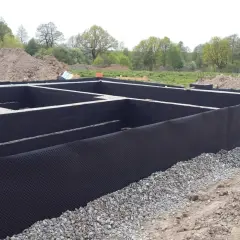 Fundament domu w budowie, z czarną izolacją i otoczakami.