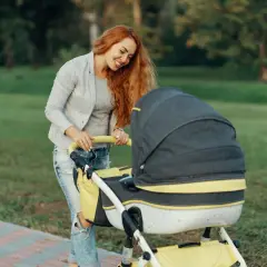 Uśmiechnięta mama z rudymi włosami pcha wózek. Idealny spacer, gdy jest 21 stopni, jak ubrać dziecko?