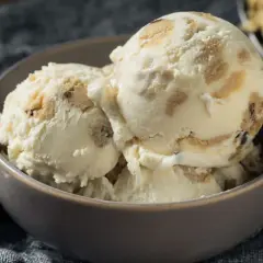 Schüssel mit cremigem Eis, durchzogen von Stückchen aus süßem Keksteig und Schokoladenstückchen. Ein Löffel liegt daneben.