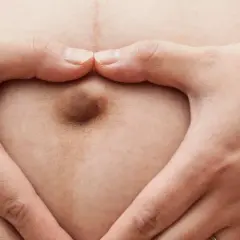 Mani a cuore circondano un ombelico in gravidanza, simbolo di amore e attesa.