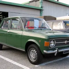 Zielony fiat 128, klasyk z lat 70., zaparkowany przed budynkiem.