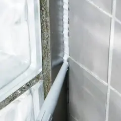 Applicator sprutar vit silikonfog längs en fog i badrummet, intill en duschvägg av glasblock.