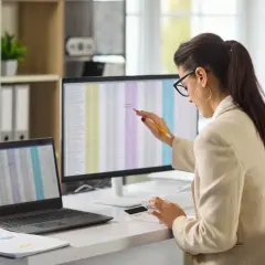 Kobieta w okularach pracuje przy komputerze, analizując dane w arkuszu kalkulacyjnym.