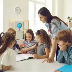 Lehrerin unterstützt Kinder bei ihrer Projektarbeit. Sie arbeiten gemeinsam an einem Buch, lernen und lachen.