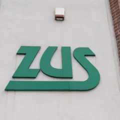 Zielone logo ZUS na jasnej ścianie budynku z ceglanymi elementami.