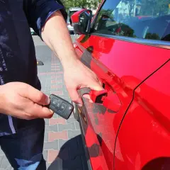 Mężczyzna z kluczykiem w dłoni otwiera czerwony samochód, korzystając z systemu keyless go.