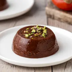 Budino di cachi al cioccolato, guarnito con pistacchi tritati, servito su un piatto bianco.