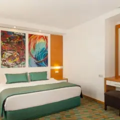 Pokój w Ladonia Hotels Adakule: łóżko z zieloną pościelą, kolorowe obrazy nad wezgłowiem, toaletka z lustrem.