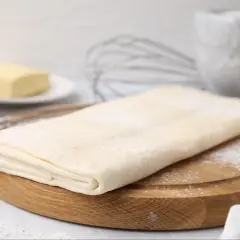 Gotowe ciasto francuskie na desce, obok masło i trzepaczka. Sprawdź, jaka jest ciasto francuskie cena!