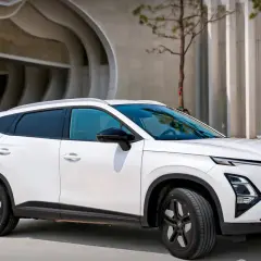 Biały OMODA hybryda zaparkowany przed nowoczesnym budynkiem. Stylowy SUV z charakterystycznym grillem i dynamiczną linią nadwozia.