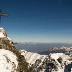 Krzyż na szczycie Gerlach, pokryty śniegiem. Widok na ośnieżone Tatry. Uważaj, by nie dostać mandatu za wejście na Gerlach bez przewodnika!