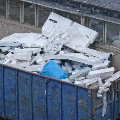 Kontener z niebieskimi workami i pociętym styropianem.