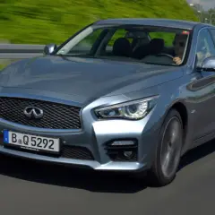 Srebrny infiniti samochód pędzi po autostradzie, kierowca w okularach przeciwsłonecznych cieszy się jazdą.