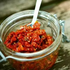 Słoik pełen aromatycznej pasty z suszonych pomidorów, gotowej do użycia. Łyżeczka zanurzona w czerwonej masie.