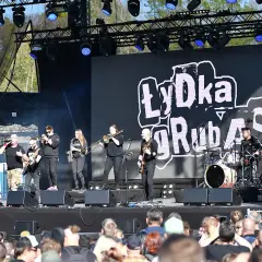 Zespół Łydka Grubasa na scenie, grający koncert. W tle wielki ekran z logo zespołu.