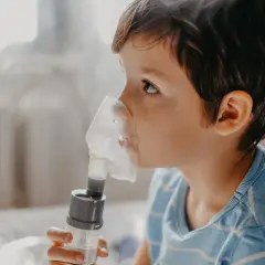 Chłopiec w masce inhalatora wykonuje inhalację solą fizjologiczną.
