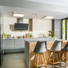Moderna cocina con isla central, gabinetes grises y de madera, campana extractora negra y tres taburetes.