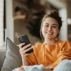 Uśmiechnięta kobieta z telefonem w dłoni, relaksująca się na kanapie. Może właśnie sprawdza księgowanie w aplikacji ING.