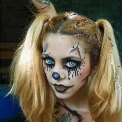 Chica con maquillaje de halloween de payaso aterrador, ojos azules brillantes, nariz de payaso y purpurina en el cabello.