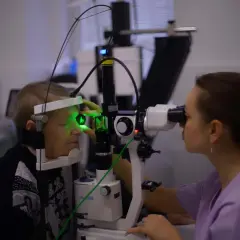 Lekarz okulista wykonuje badanie oka pacjentki przy użyciu mikroskopu szczelinowego, przygotowując się do zabiegu kapsulotomii.