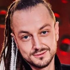 Aleksander Baron z dredami i brodą, na czerwonym tle.