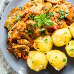 Pyszny gulasz z indyka w sosie z pieczarkami i papryką, podany z kluskami śląskimi posypanymi natką pietruszki.