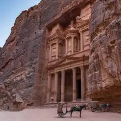 Skaliste klify Petry, Jordania, z wykutym w skale Skarbcem. Dwa wozy zaprzężone w osły czekają na turystów, marzących o jordania loty.