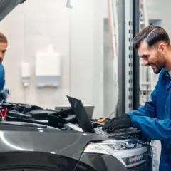Mechanicy diagnozują drgania silnika na wolnych obrotach diesel, jeden sprawdza pod maską, drugi analizuje dane na laptopie.