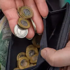 Dłoń z monetami i banknotami w portfelu. Zastanawiasz się, ile wynosi renta wojskowa?