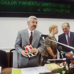 Uroczystość otwarcia, gdzie powstała pierwsza polska giełda. Mężczyzna w szarym garniturze prezentuje pudełko z szelkami.