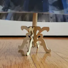 Base de un maniquí 3d de madera con un soporte ornamental, sosteniendo una falda de tela brillante.