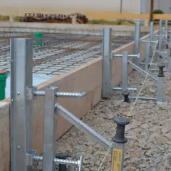 Stahlstützen und Holzbretter bilden die schalung wand für eine Betonplatte. Bewehrungsstahl und grüne Rohre sind sichtbar.