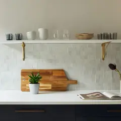 A kitchen backsplash features zellige tile, a Moroccan mosaic of hand-cut, glazed tiles. A wooden cutting board with a plant sits on the counter.