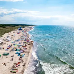 Tłum ludzi na plaży w Darłowie, gdzie można zwiedzić piękne wybrzeże i kąpać się w morzu.