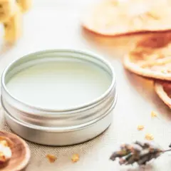 Ein Döschen mit selbstgemachtem Lippenbalsam, umgeben von getrockneten Orangen, Lavendel und Kräutern.