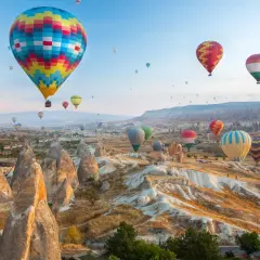 Balony na gorące powietrze unoszące się nad skalistym krajobrazem Kapadocji o wschodzie słońca.