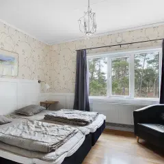 Mysigt rum på vandrarhem Gotland med två sängar, fåtölj och fönster med utsikt över skog.