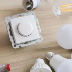 Ściemnianie led: biały ściemniacz, żarówki led, puszka instalacyjna i śrubokręt na drewnianym blacie.