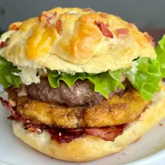 Domowy hamburger z serem, bekonem, sałatą i panierowanym kotletem na talerzu.