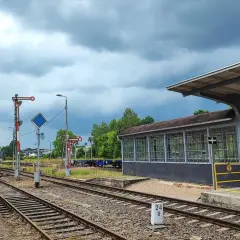 Tory kolejowe na stacji Starogard Gdański pod pochmurnym niebem. Widać peron, budynek poczekalni i semafory.