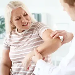 Lekarz bada łokieć pacjentki, która odczuwa ból i napięcie mięśni.
