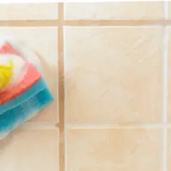 Mano con guanto giallo che pulisce le piastrelle del bagno con una spugna bagnata di schiuma.