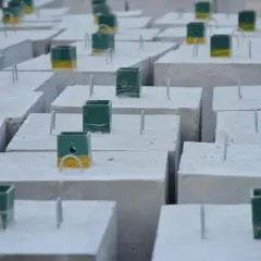 Szare bloczki betonowe z zielono-żółtymi elementami i metalowymi prętami, czekające na dalsze prace budowlane.