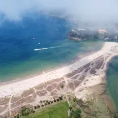 Vista aérea de la playa de Miño, con arena dorada, mar azul y verde, y casas costeras.