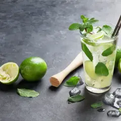 Orzeźwiający mohito smak: szklanka z lodem, limonkami i miętą, obok wyciśnięta limonka i tłuczek.