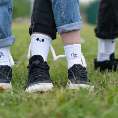 Jak nosić długie skarpety? Zabawne białe skarpety z postaciami i czarne trampki na trawie.