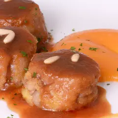 Deliciosas manitas de cerdo rellenas, bañadas en salsa y decoradas con piñones y perejil, acompañadas de puré de zanahoria.