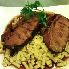 Tranches de brasato al barolo, tendres et savoureuses, servies sur un lit de pâtes fraîches, garnies de persil.