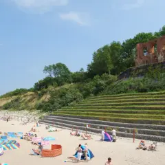 Plaża w Rewalu z ruinami na klifie. Ludzie odpoczywają na piasku, ciesząc się słońcem i widokiem. To popularne rewal atrakcje.